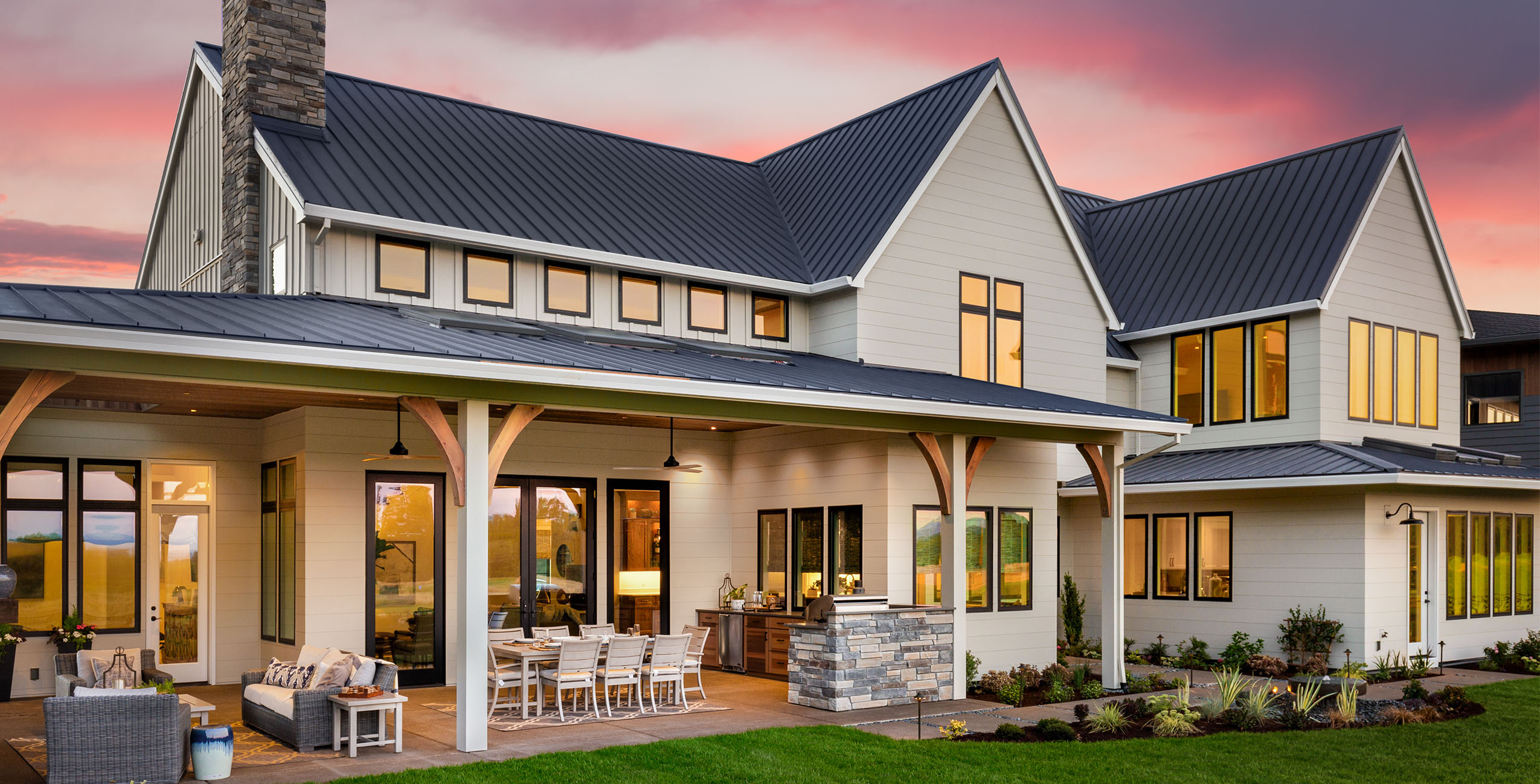 Beautiful luxury home exterior at sunset, featuring large covered patio with outdoor kitchen and barbecue